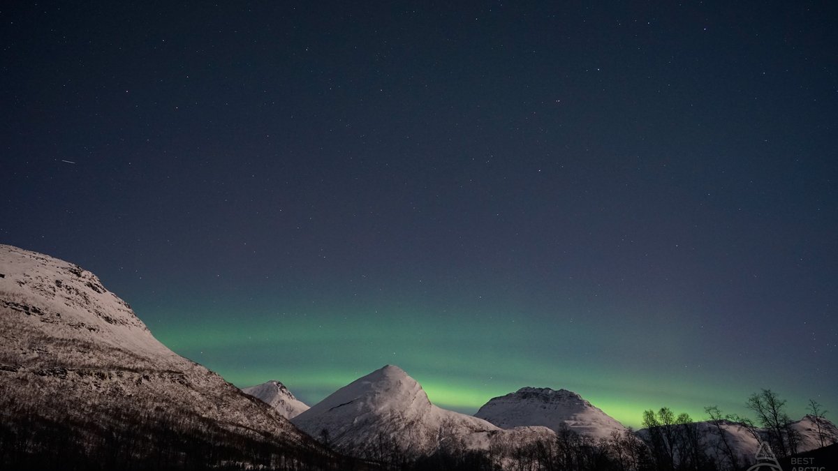 Aurora borealis over snow-covered mountains near Tromsø during polar night in mid-December