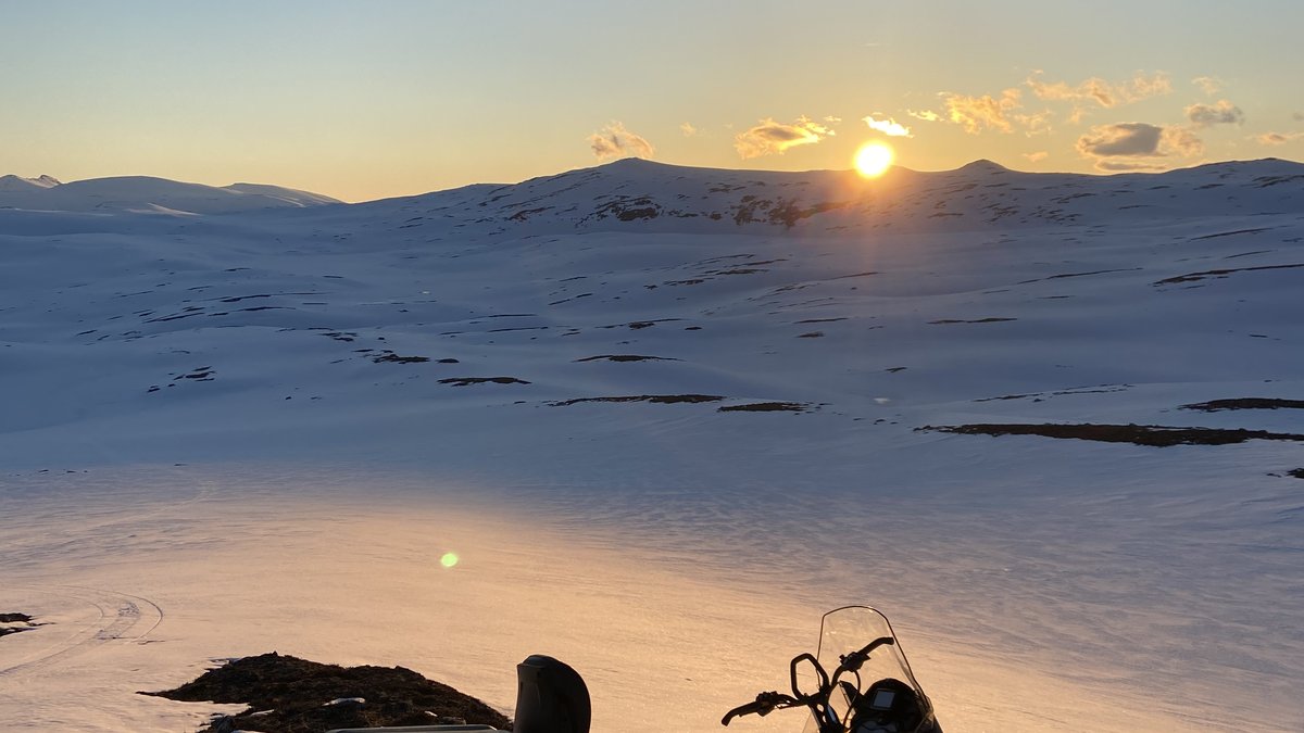 Snowmobile parked on a ridge with low Arctic sun over snow-covered mountains in late winter