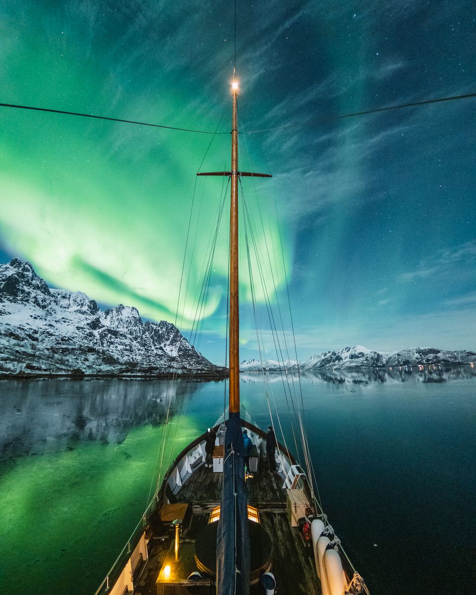 Aurora borealis over a fjord and snow-capped mountains seen from the deck of a sailing boat near Tromsø