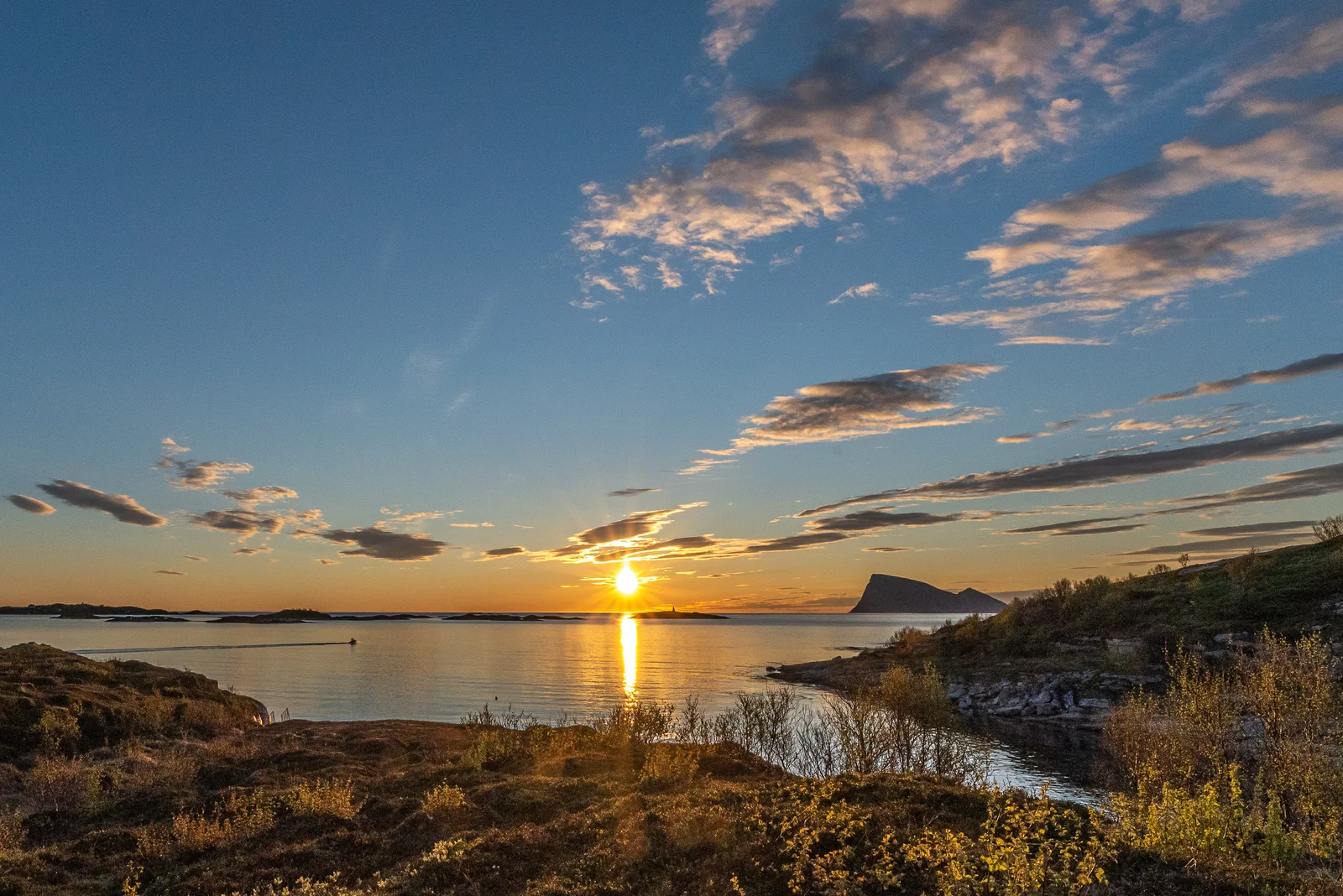 Midnight sun low on the horizon over the sea off Tromsø, with the silhouette of Håja island in the distance