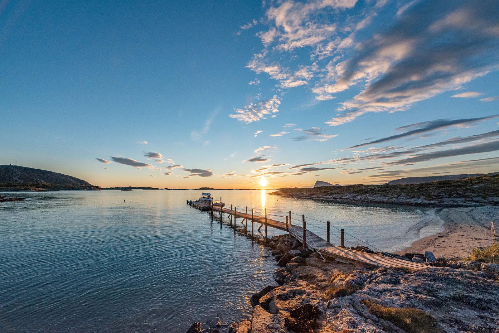 Wooden jetty and white sand beach on Sommarøy island west of Tromsø, with midnight sun reflecting across the calm water