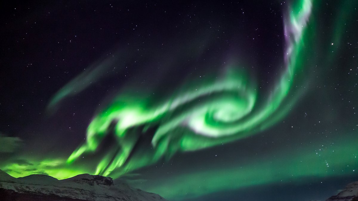 Green aurora swirling above snow-covered mountains in the Tromsø region