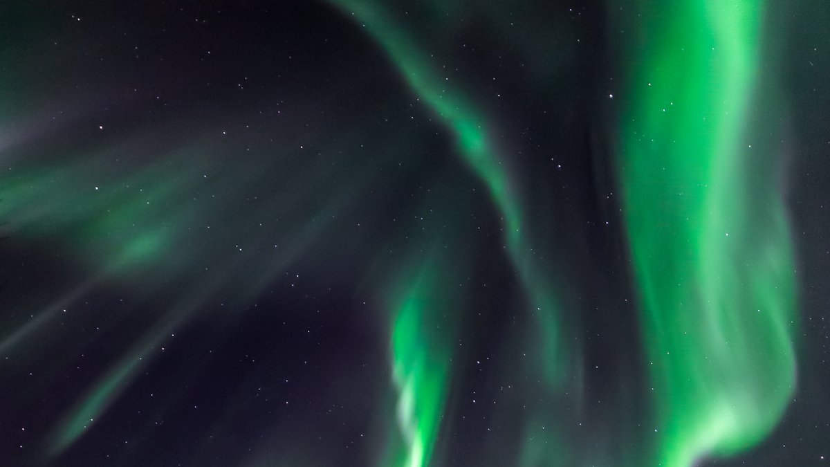 Vivid green aurora cascading over snow-covered peaks in northern Norway
