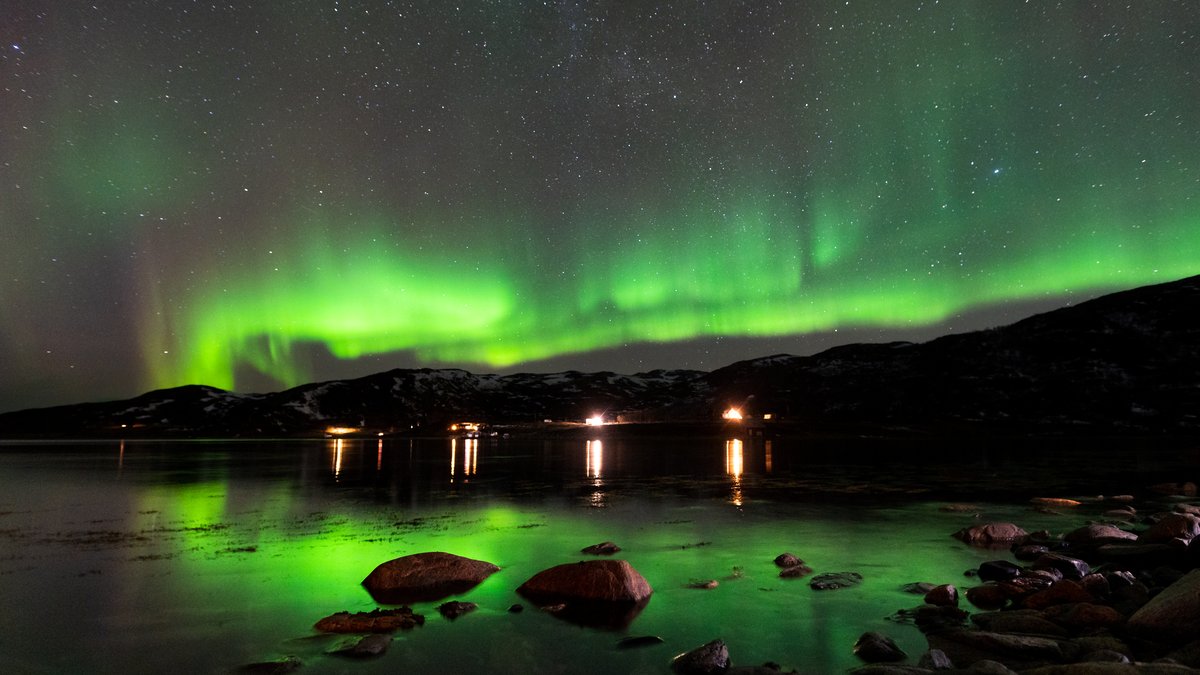 Aurora reflecting in a fjord outside Tromsø with village lights on the shore