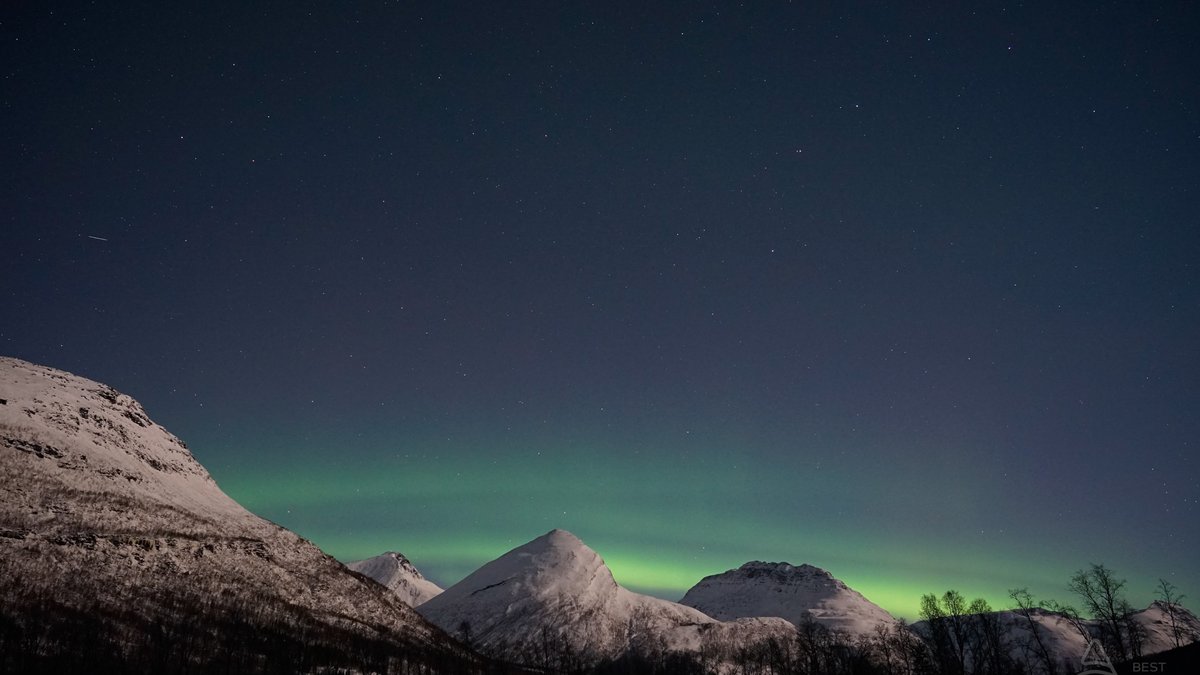 Northern lights arc over snow-covered mountains near Tromsø in winter
