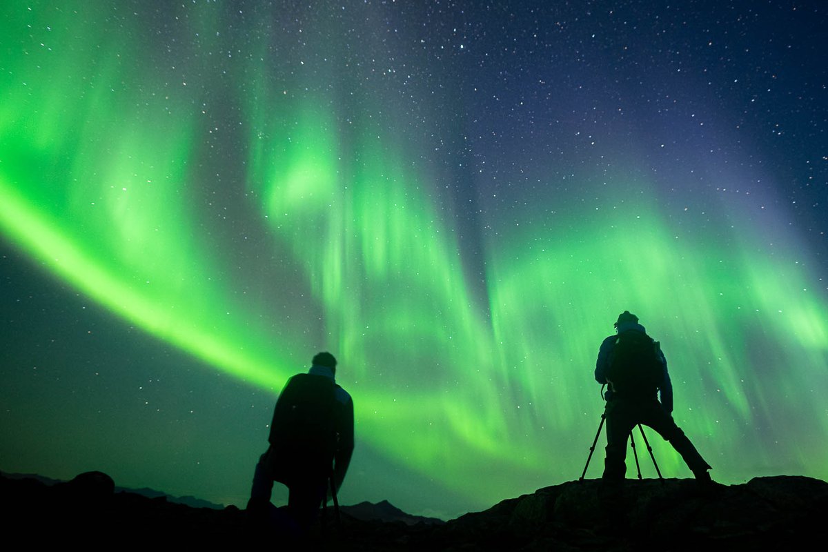 Two photographers shooting bright green northern lights from a ridge near Tromsø