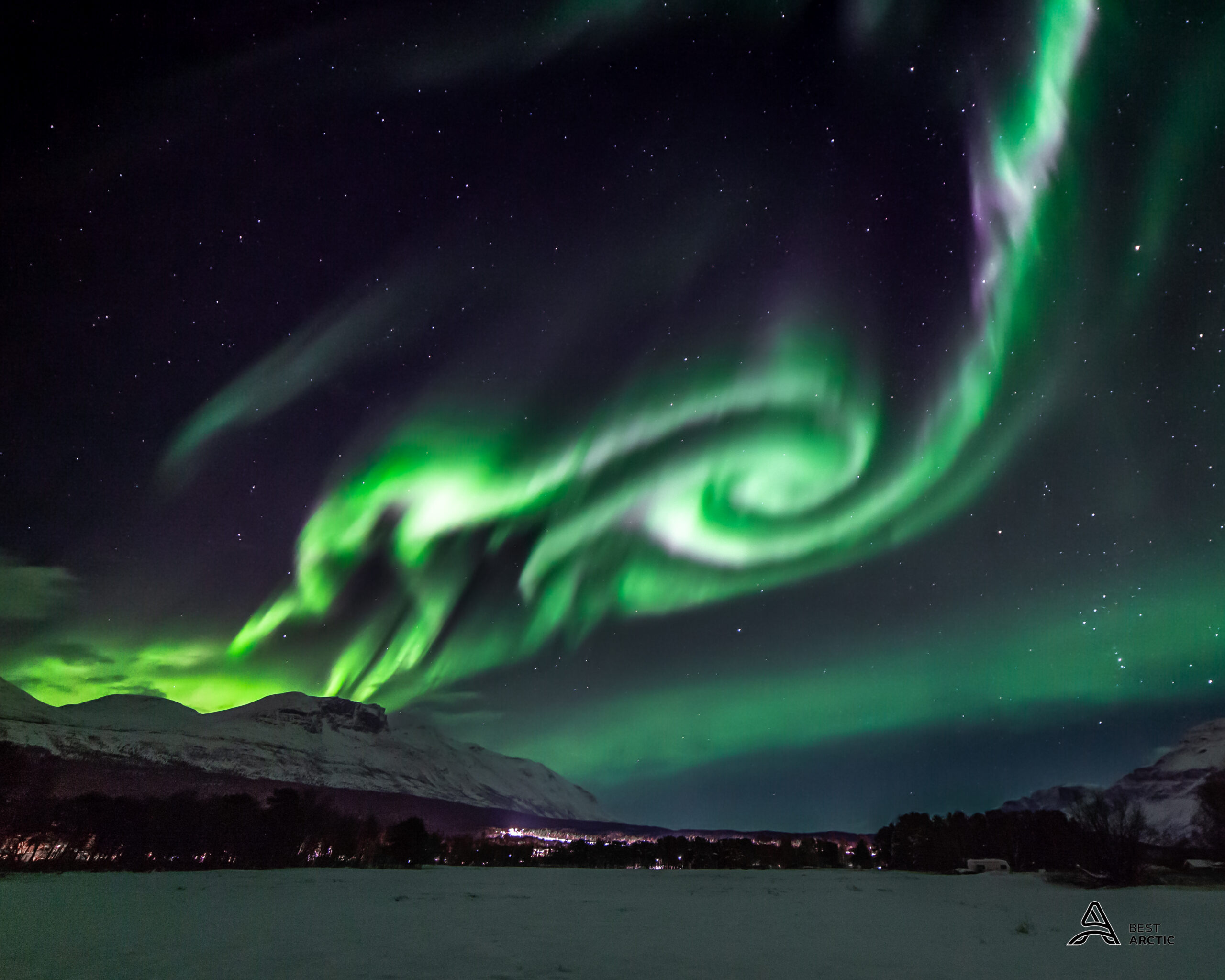 Green aurora spiralling over snow-covered mountains near Tromsø in December
