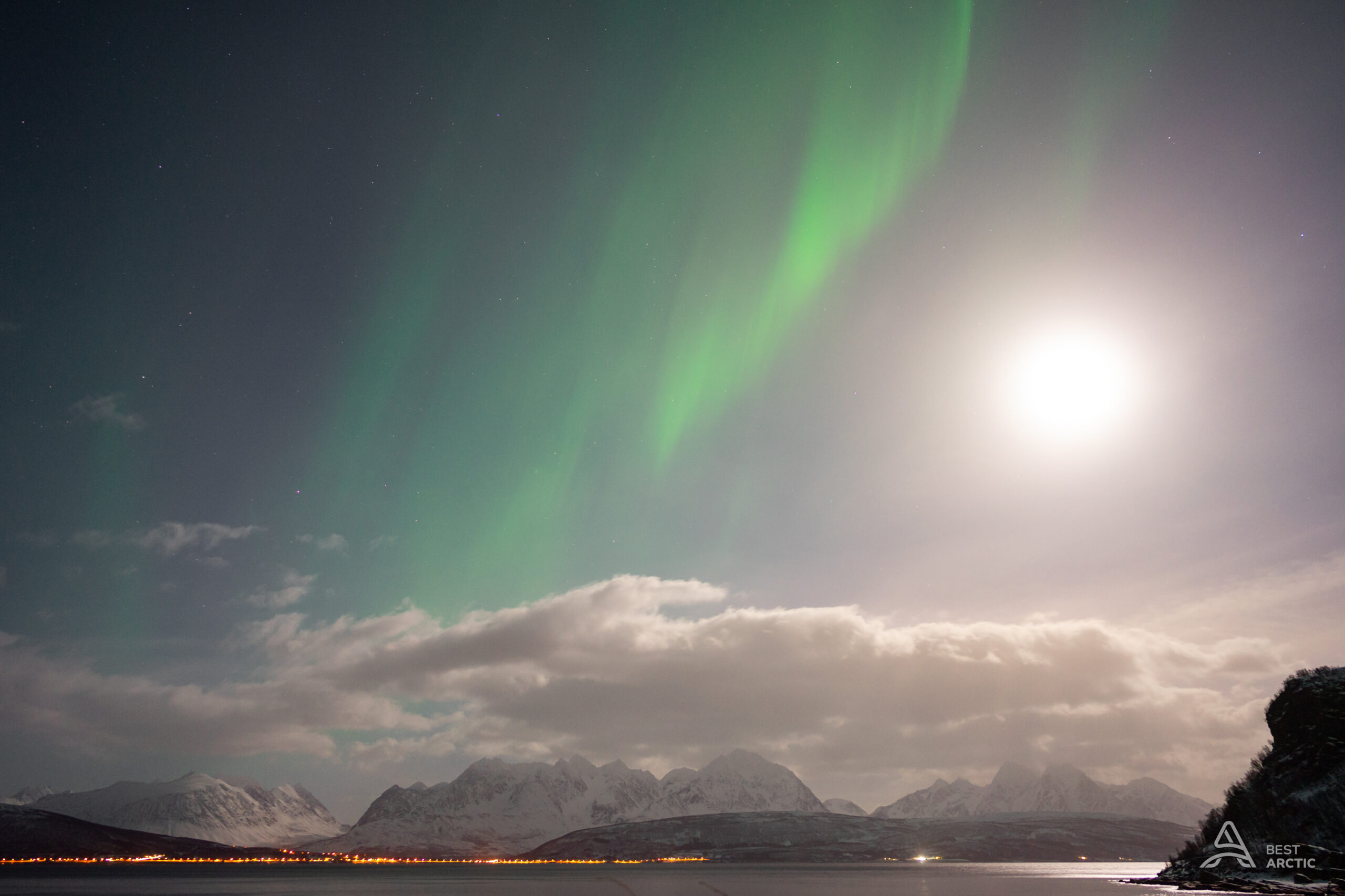 Green aurora and a bright moon over the snow-covered Lyngen Alps near Tromsø