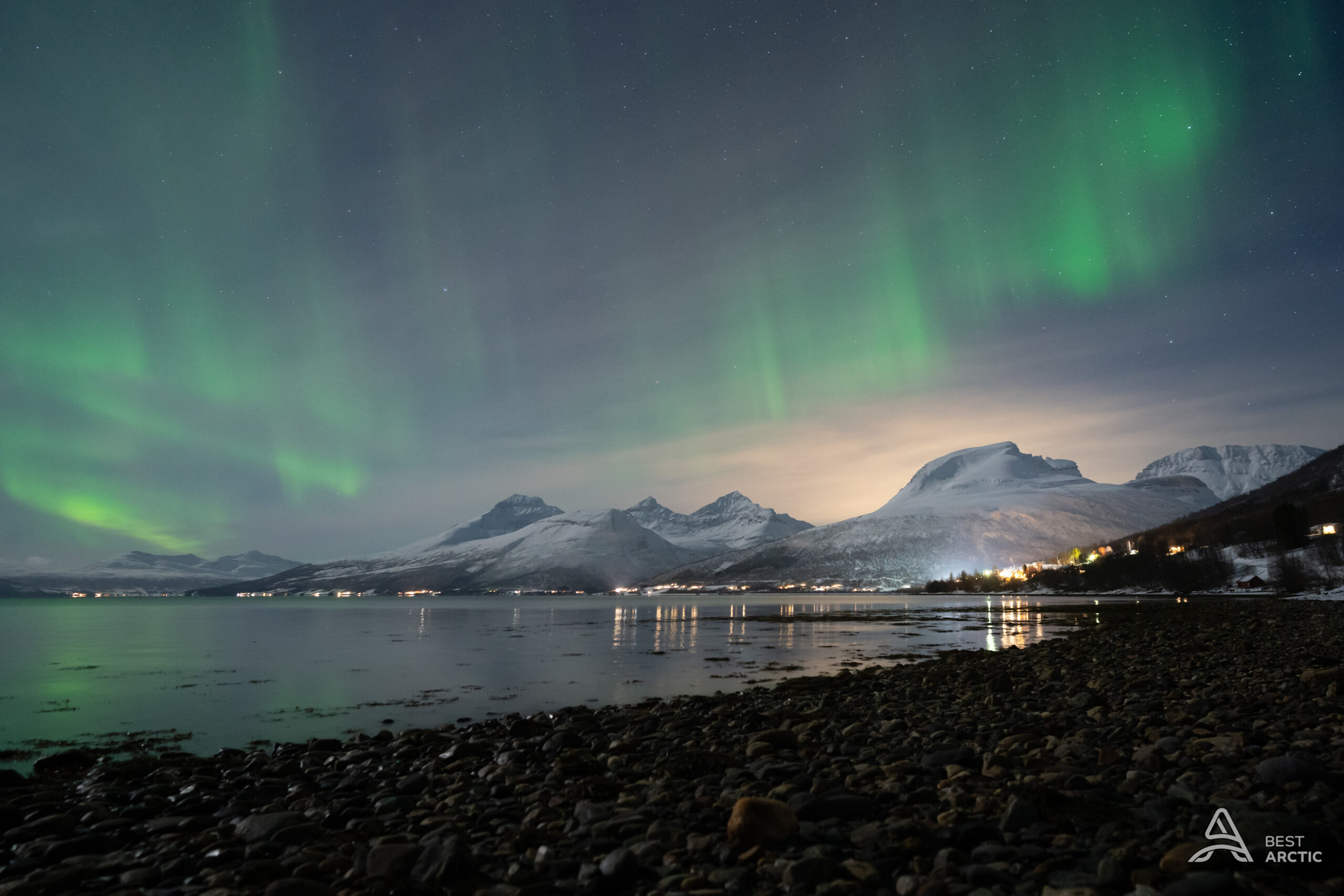 Green aurora over snow-covered mountains and a fjord near Tromsø in January